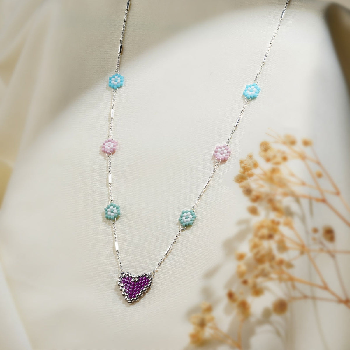 Close-up of pastel beaded daisies and silver-edged purple heart on silver bar-link chain