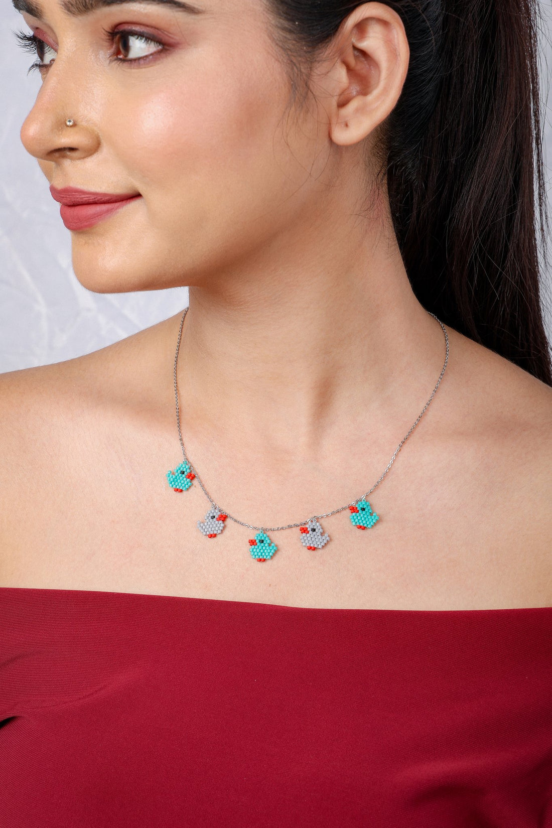 Silver tone chain necklace with five turquoise and grey beaded duckling charms on a model