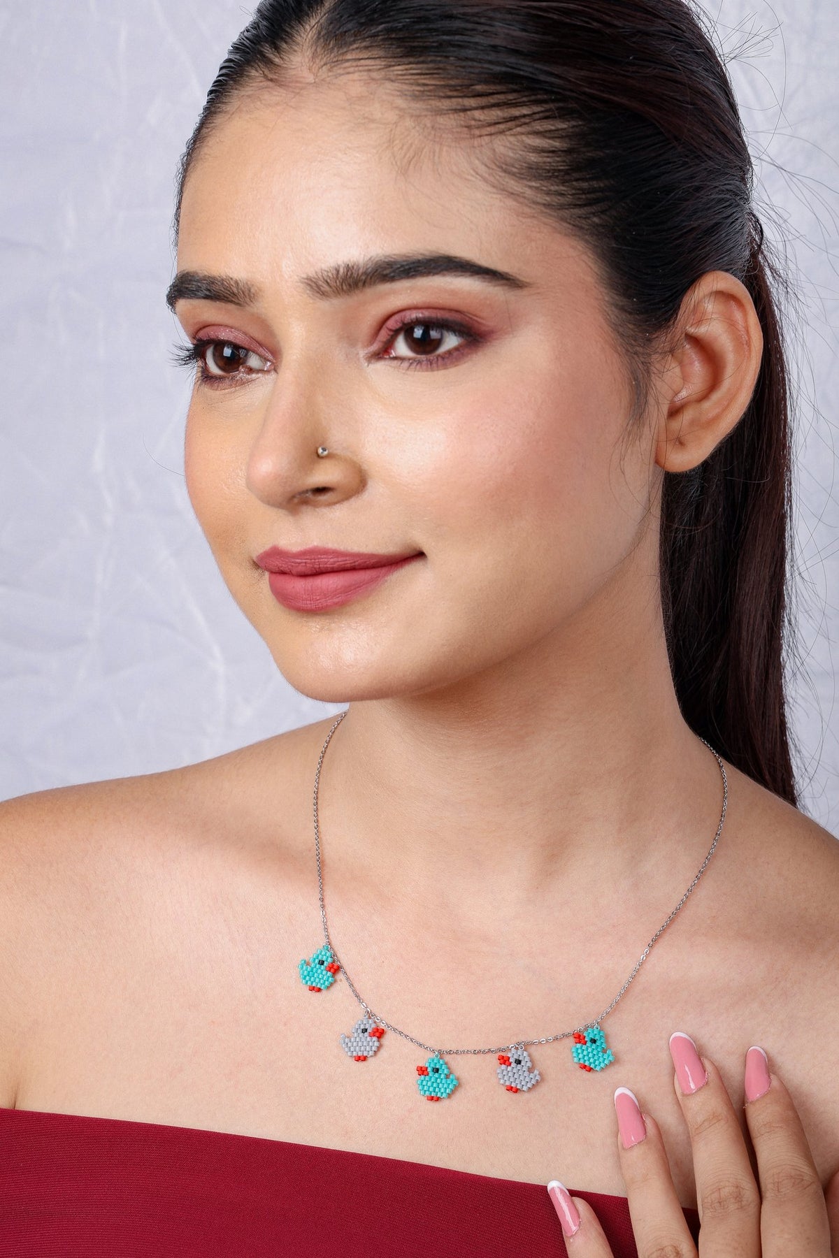 Smiling model in a red off-shoulder top wearing a duckling charm necklace
