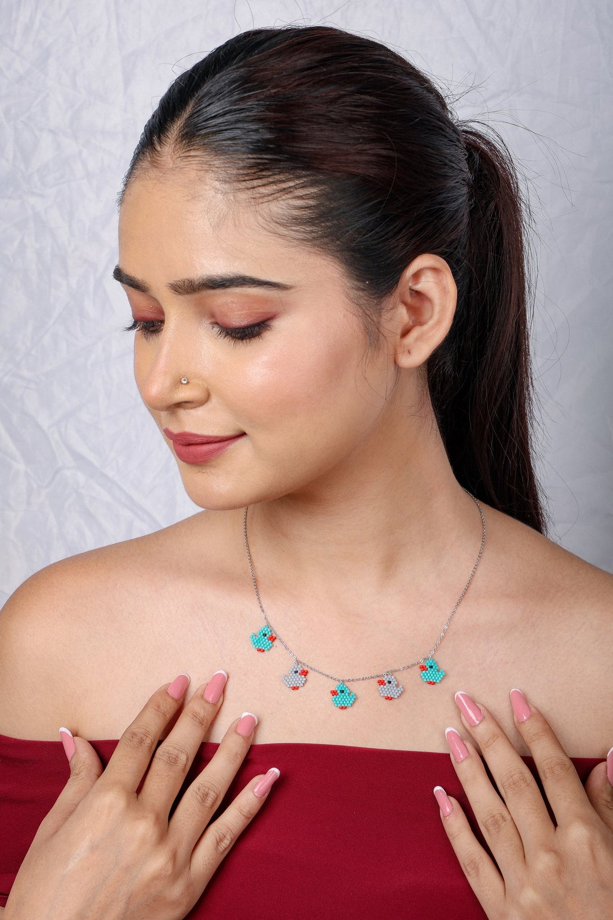 Duckling charm necklace worn with a red top, model's hand resting at the neckline