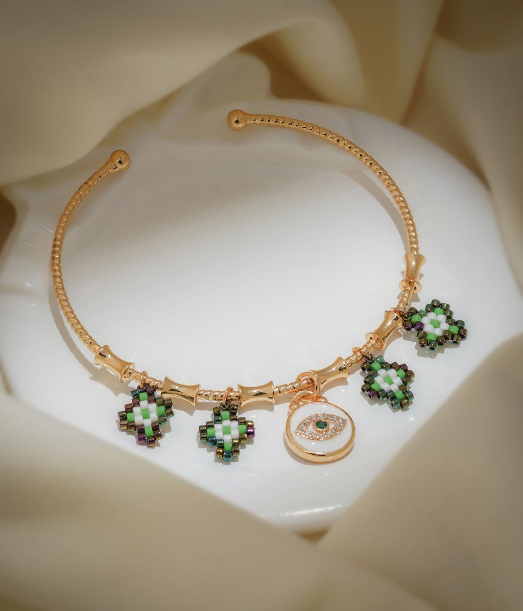 Gold open bangle with green and white beaded charms and a white evil-eye disc charm on cream silk