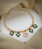 Gold open bangle with green and white beaded charms and a white evil-eye disc charm on cream silk