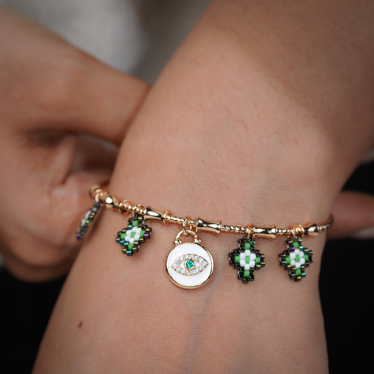 Gold evil-eye charm bangle worn on the wrist with green beaded diamond charms