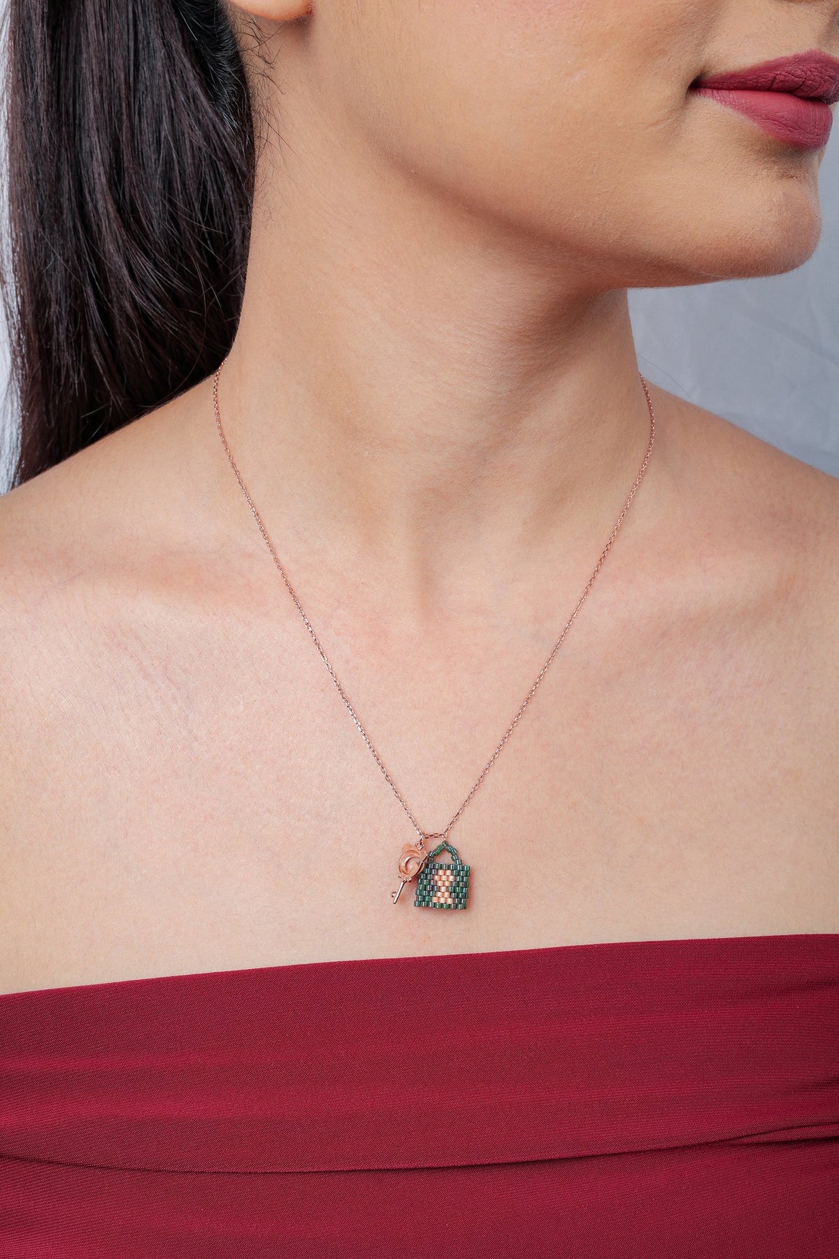 Model wearing rose-gold chain with green beaded padlock pendant and small key charm