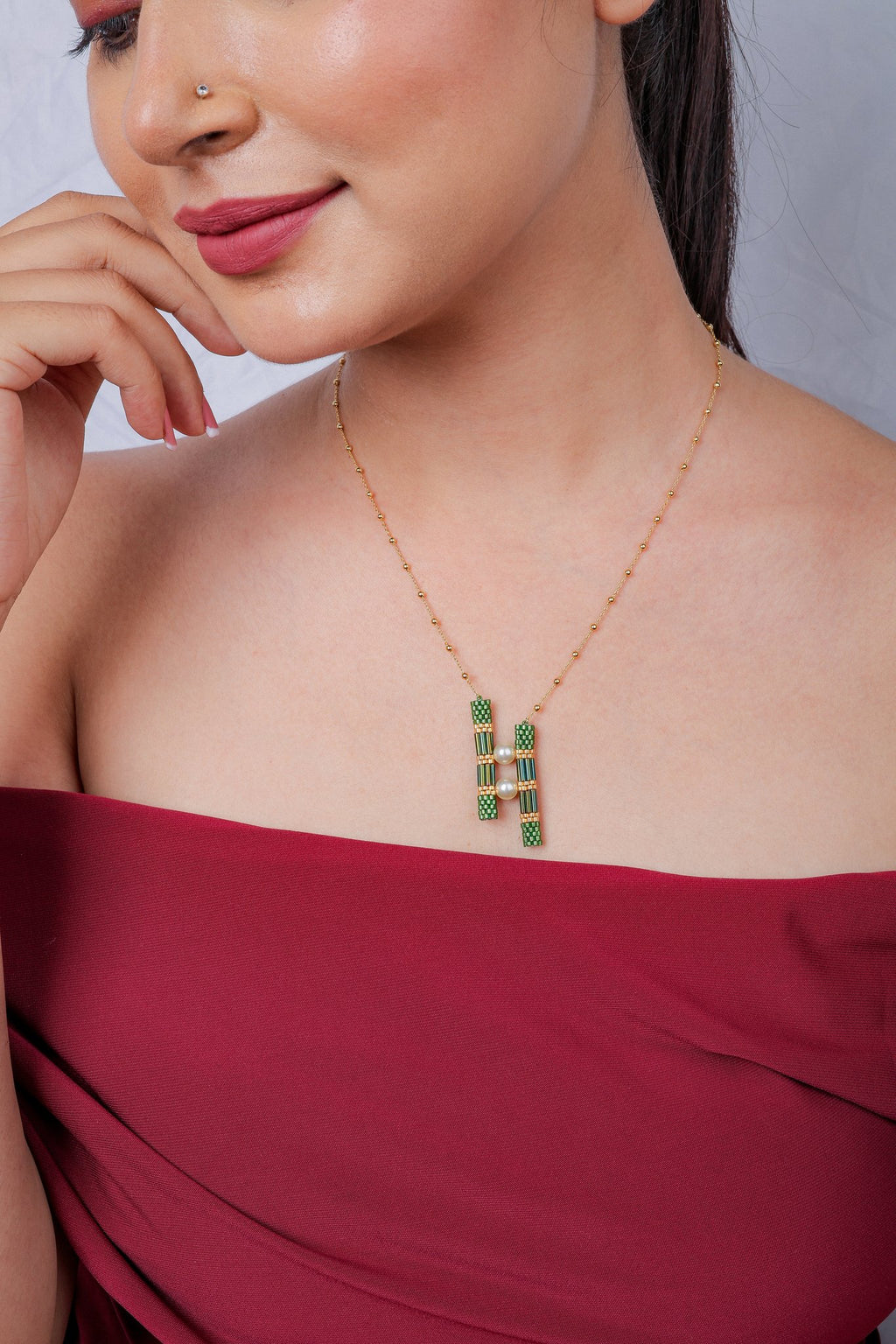 Model in a red off-shoulder top wearing a green twin bar pendant necklace