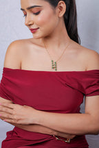 Emerald beaded bar pendant on a fine gold-tone chain, model looking down in a red top