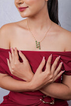 Green and gold twin bar pendant worn with a red off-shoulder top, arms crossed