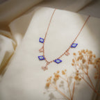 Rose-gold charm necklace with cobalt beaded evil-eye charms and butterfly charms on cream fabric