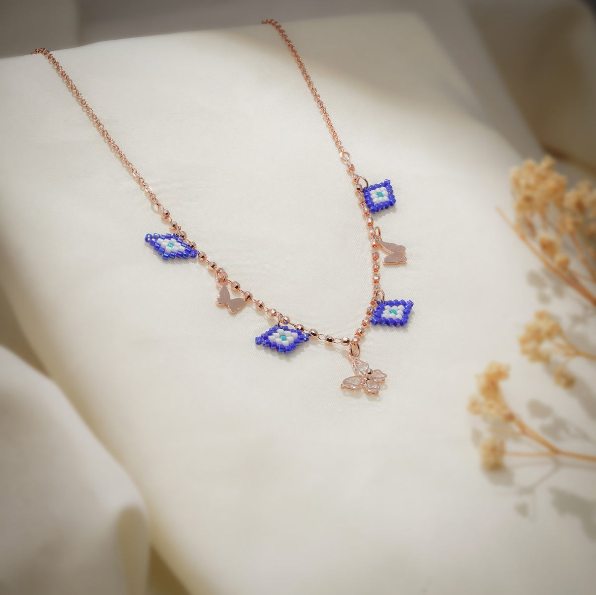 Angled view of cobalt evil-eye charms, rose-gold butterflies and crystal butterfly on a faceted chain