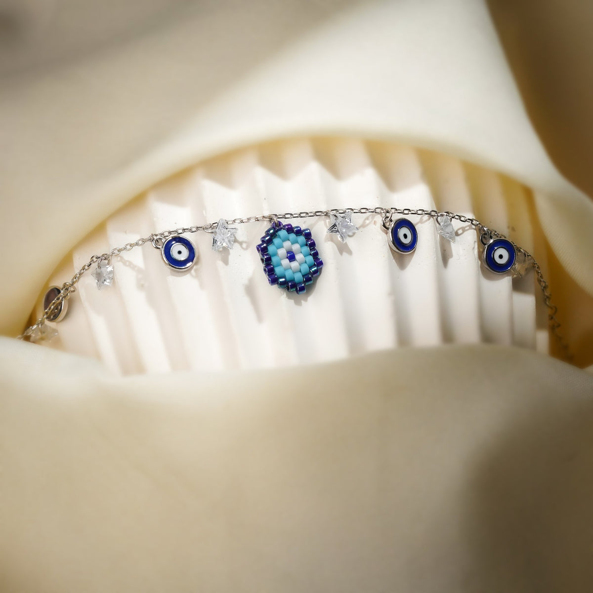 Silver evil eye bracelet draped over a ribbed white stand with crystal stars and eye charms