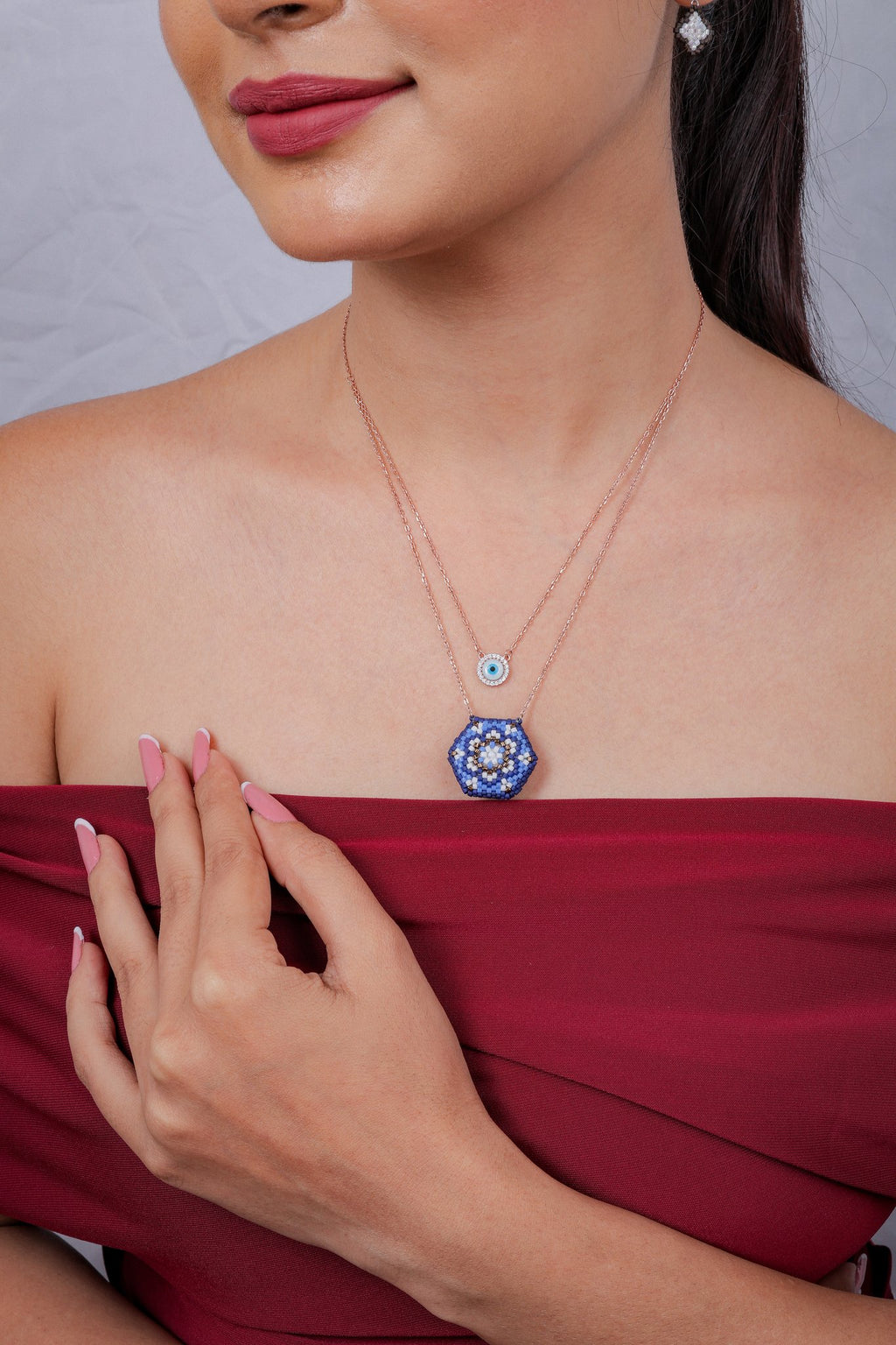 Model in a red top wearing a two-tier evil-eye and blue mandala pendant necklace
