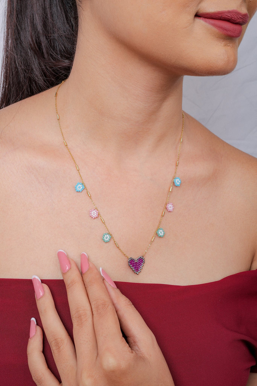 Model wearing gold necklace with pastel blue, pink and mint flower charms and fuchsia heart