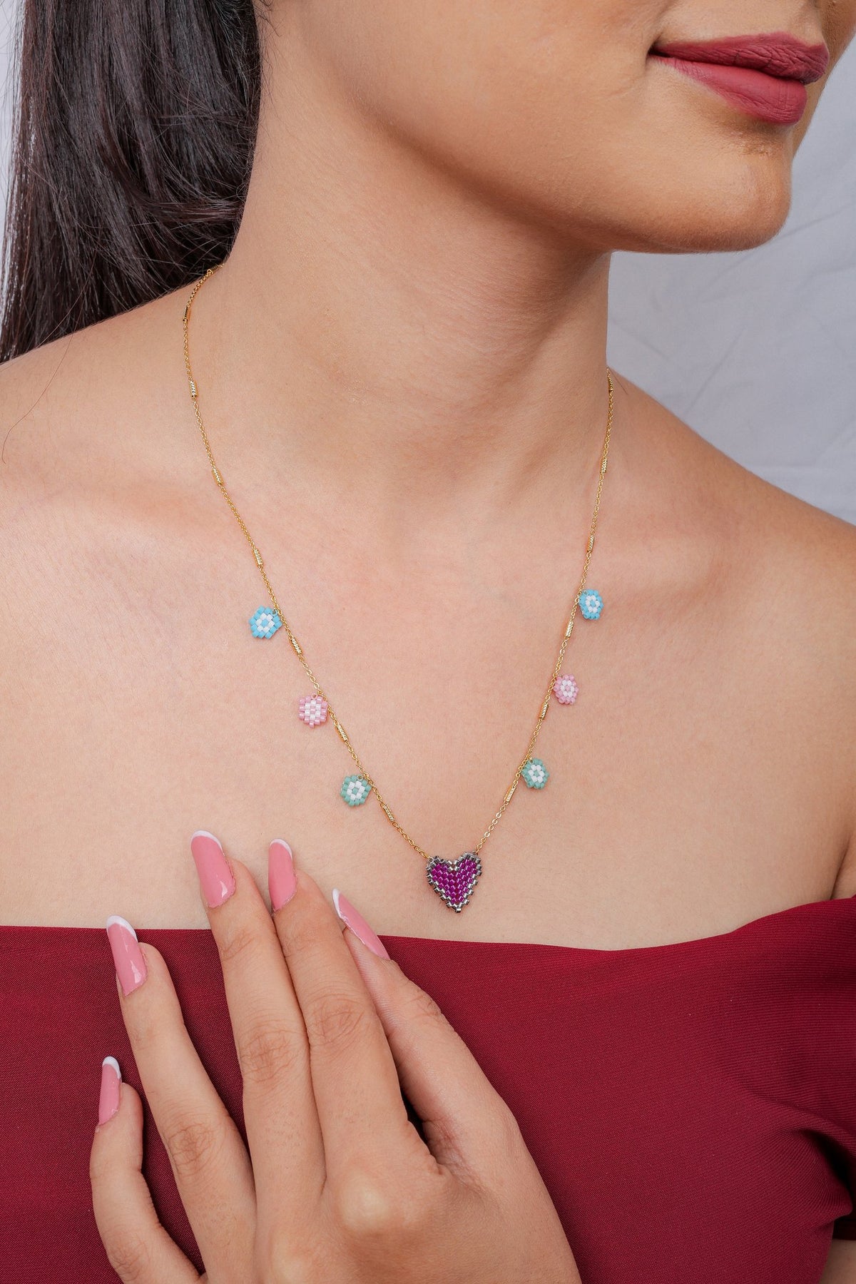 Model wearing gold necklace with pastel blue, pink and mint flower charms and fuchsia heart