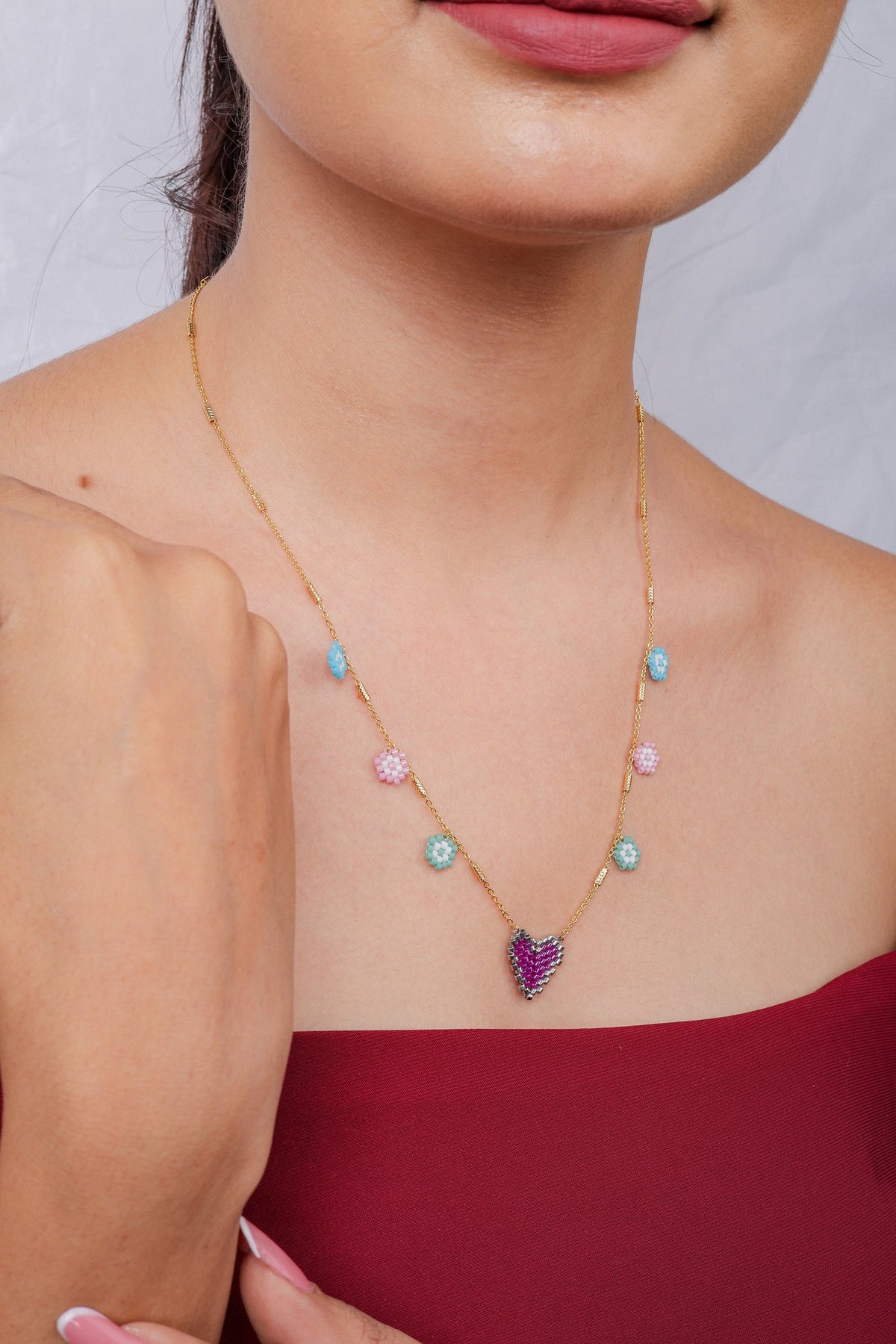 Side view of model wearing gold chain with pastel flower charms and fuchsia beaded heart