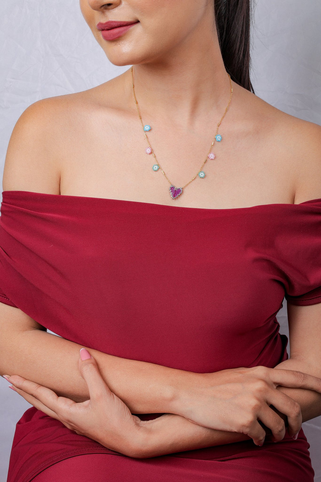 Model in red off-shoulder dress wearing gold heart and flower charm necklace