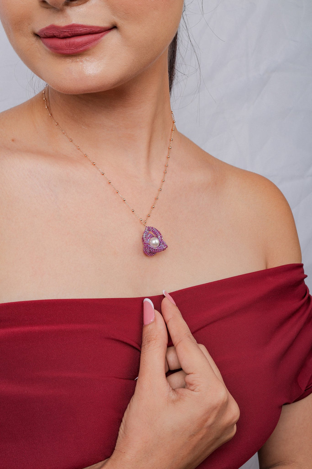 Model in a red off-shoulder top wearing a fuchsia knot pendant necklace