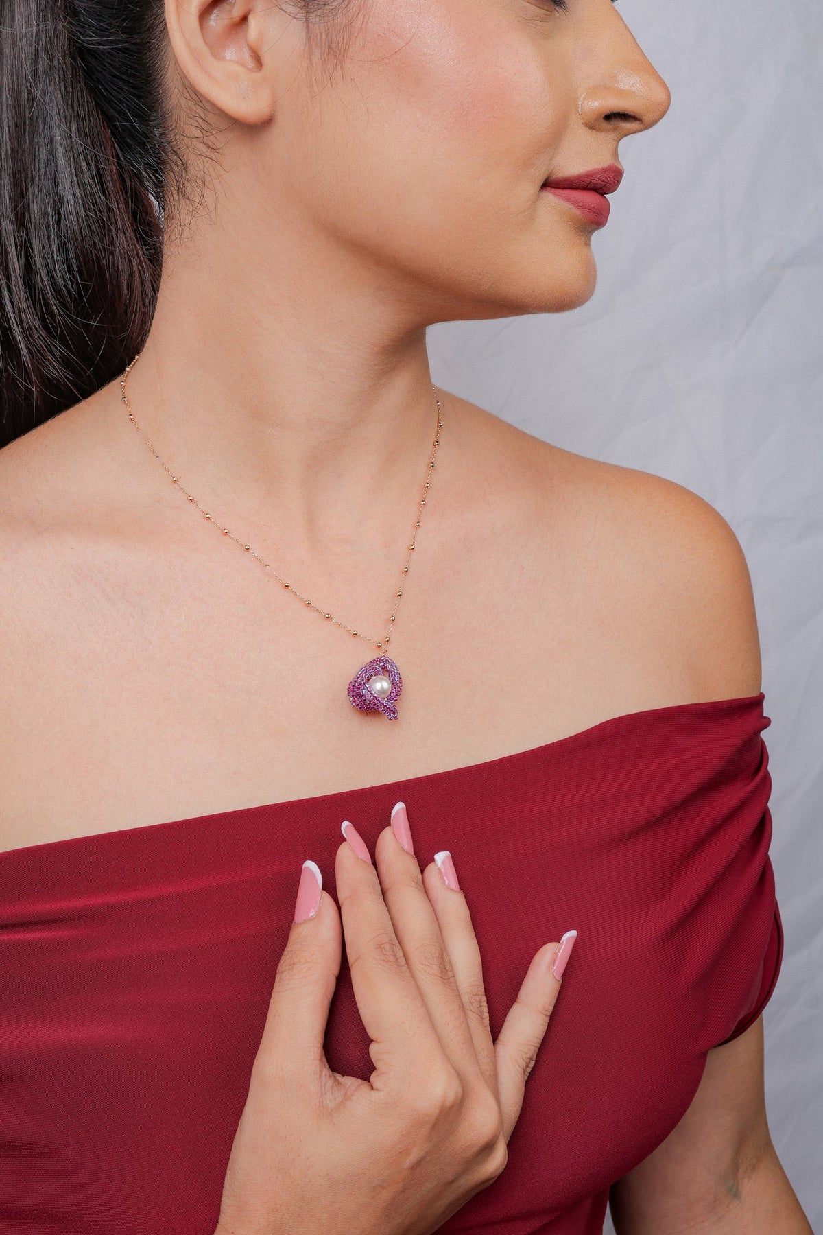 Side profile of a model wearing a rose-gold-tone chain with a fuchsia beaded knot pendant