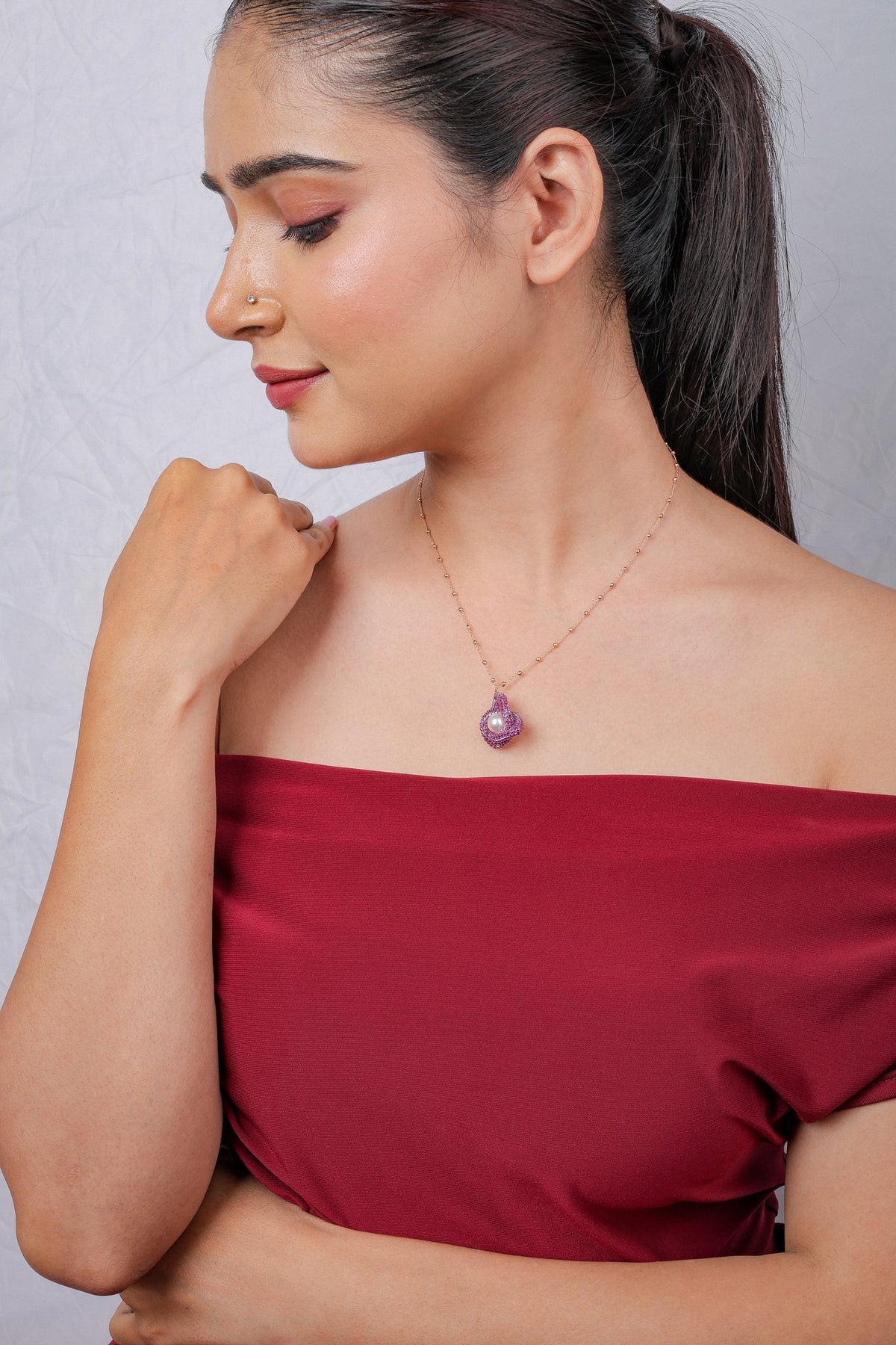 Model glancing down, wearing a small fuchsia and pearl knot pendant on a rose-gold-tone chain