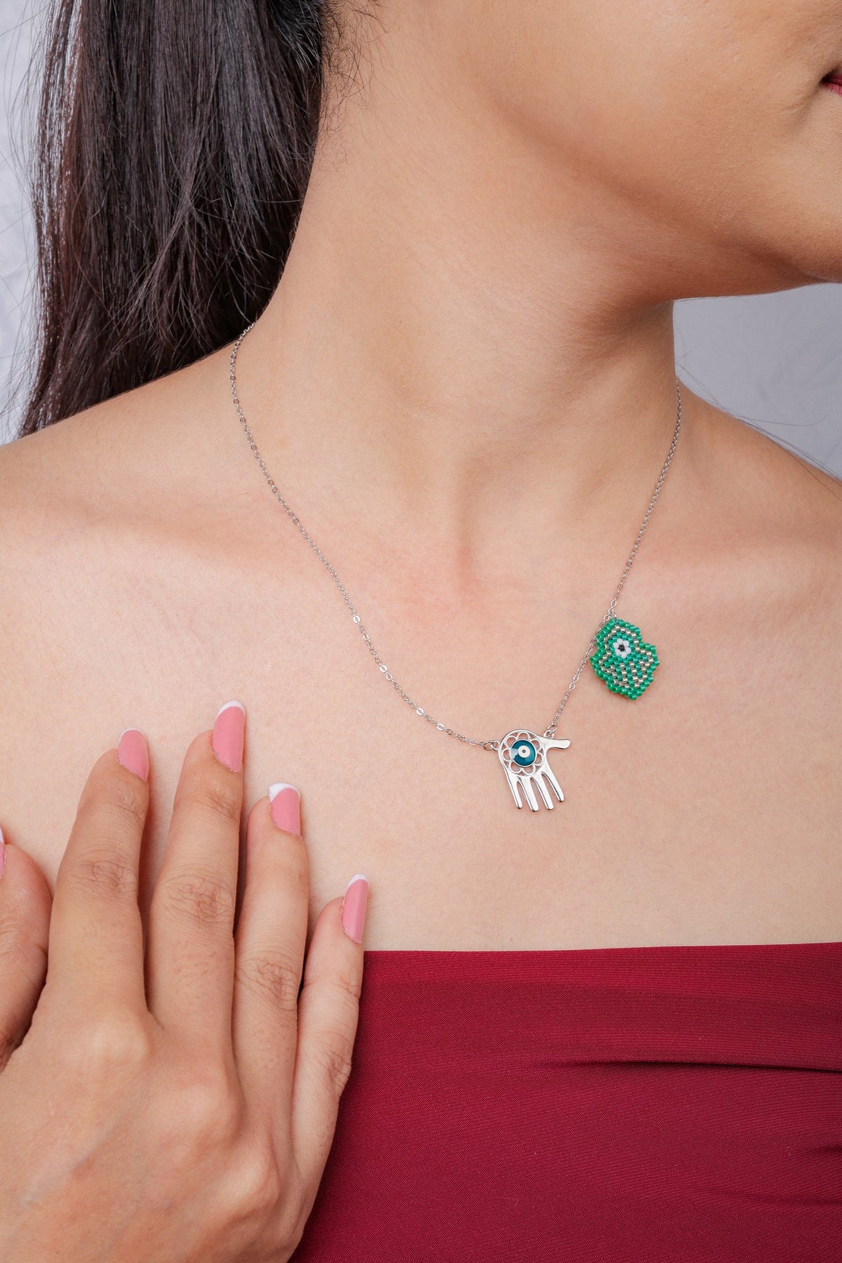 Close view of silver hand charm with teal evil eye beside green beaded hamsa charm on the model