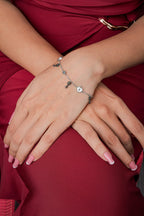 Silver lock and key charm bracelet on the wrist, hands resting on red fabric