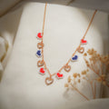 Rose-gold chain necklace with red and navy pixel-heart charms and crystal open hearts on cream silk