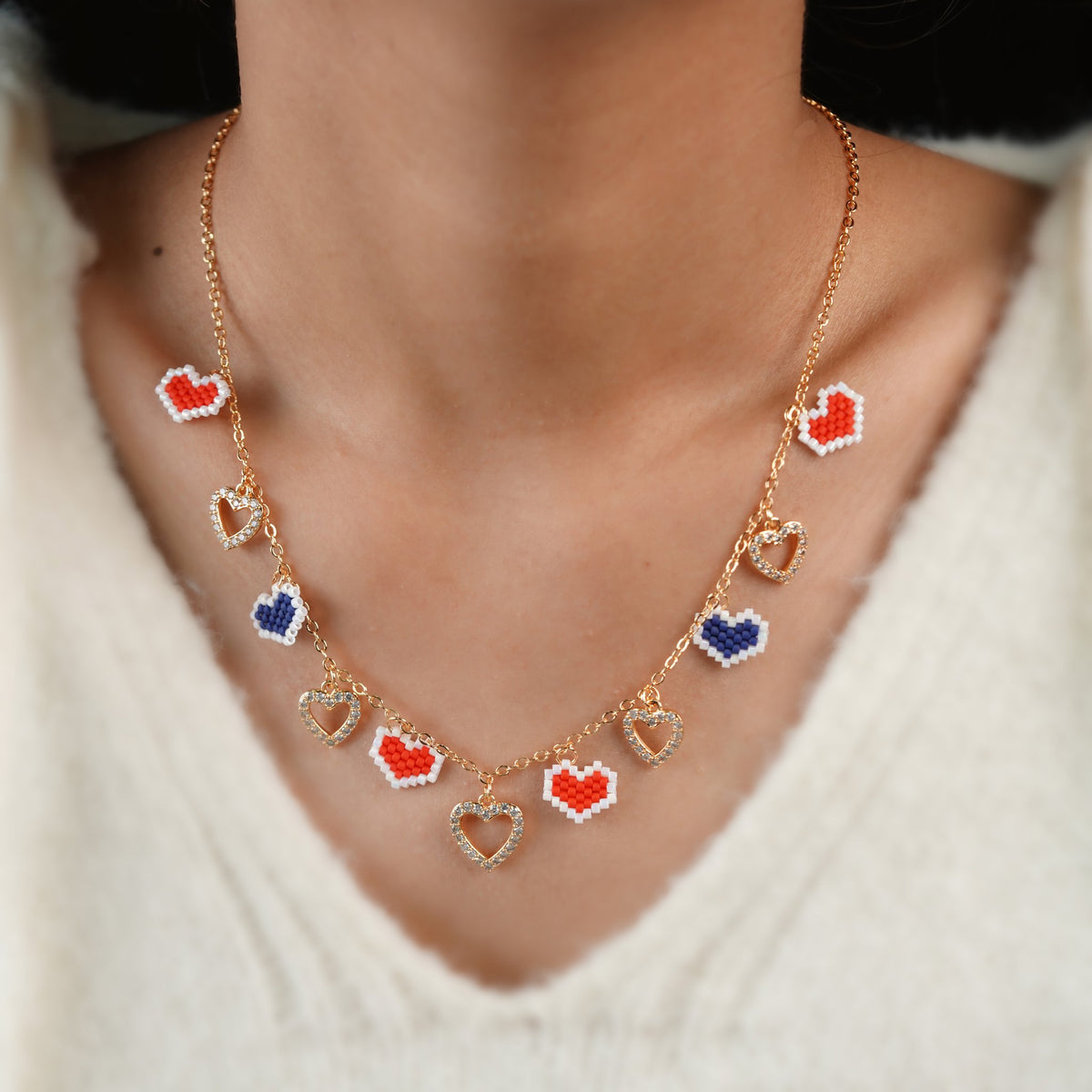 Model wearing rose-gold necklace with red and navy beaded hearts and crystal open-heart charms