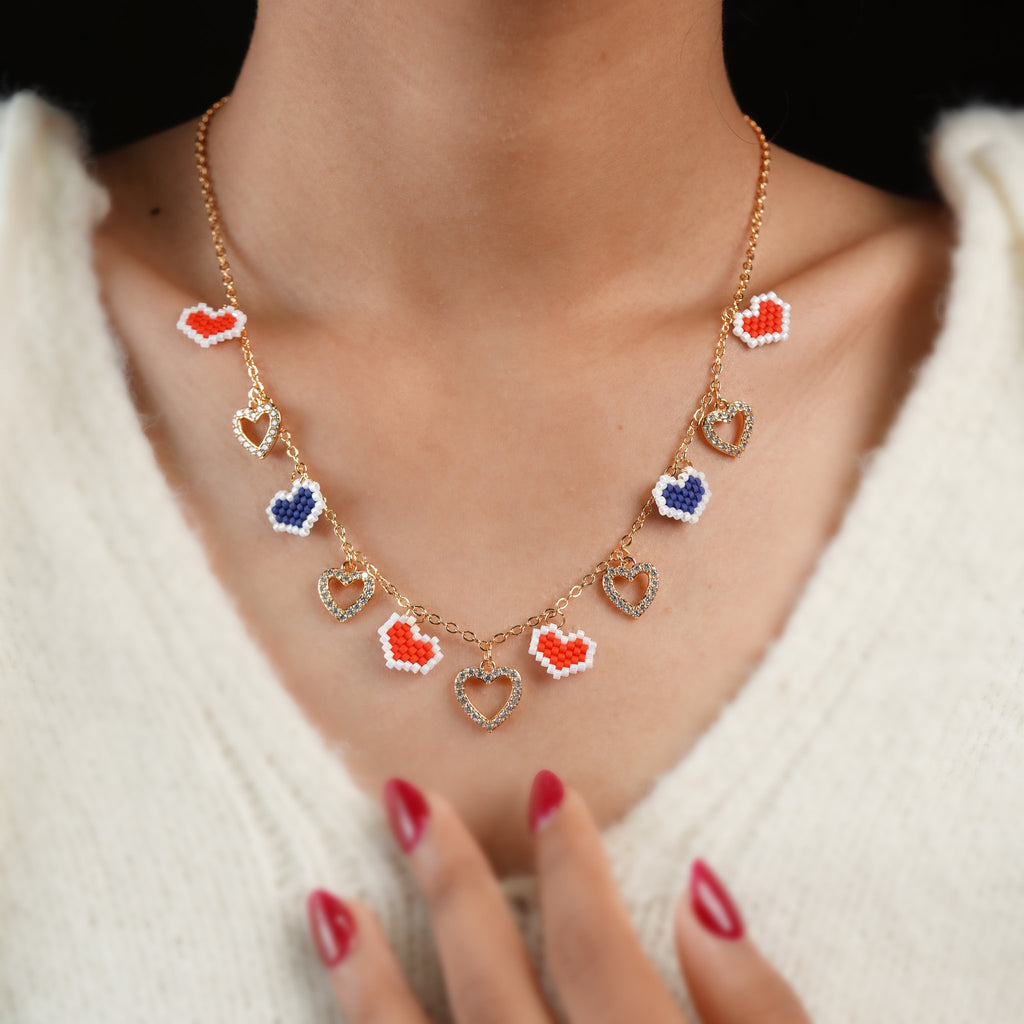 Rose-gold heart charm necklace worn with a cream knit, red and navy beaded hearts along the chain