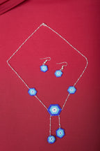 Silver evil eye necklace with five beaded blue hexagons and matching hook earrings on red fabric