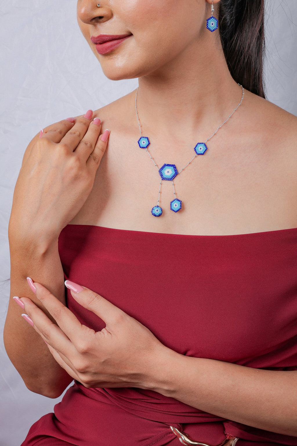 Model in red dress wearing silver chain with beaded evil eye hexagons and hexagon earring