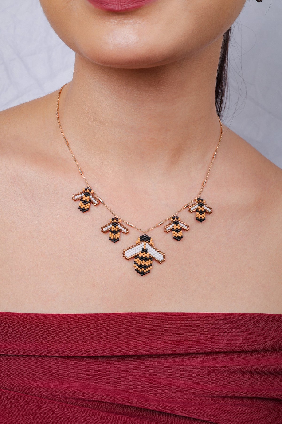 Model wearing rose-gold necklace with five beaded bees in black, amber and white