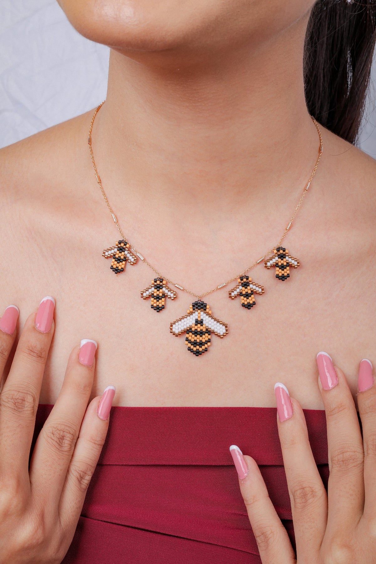 Model framing collarbone with both hands, wearing beaded honeybee charm necklace