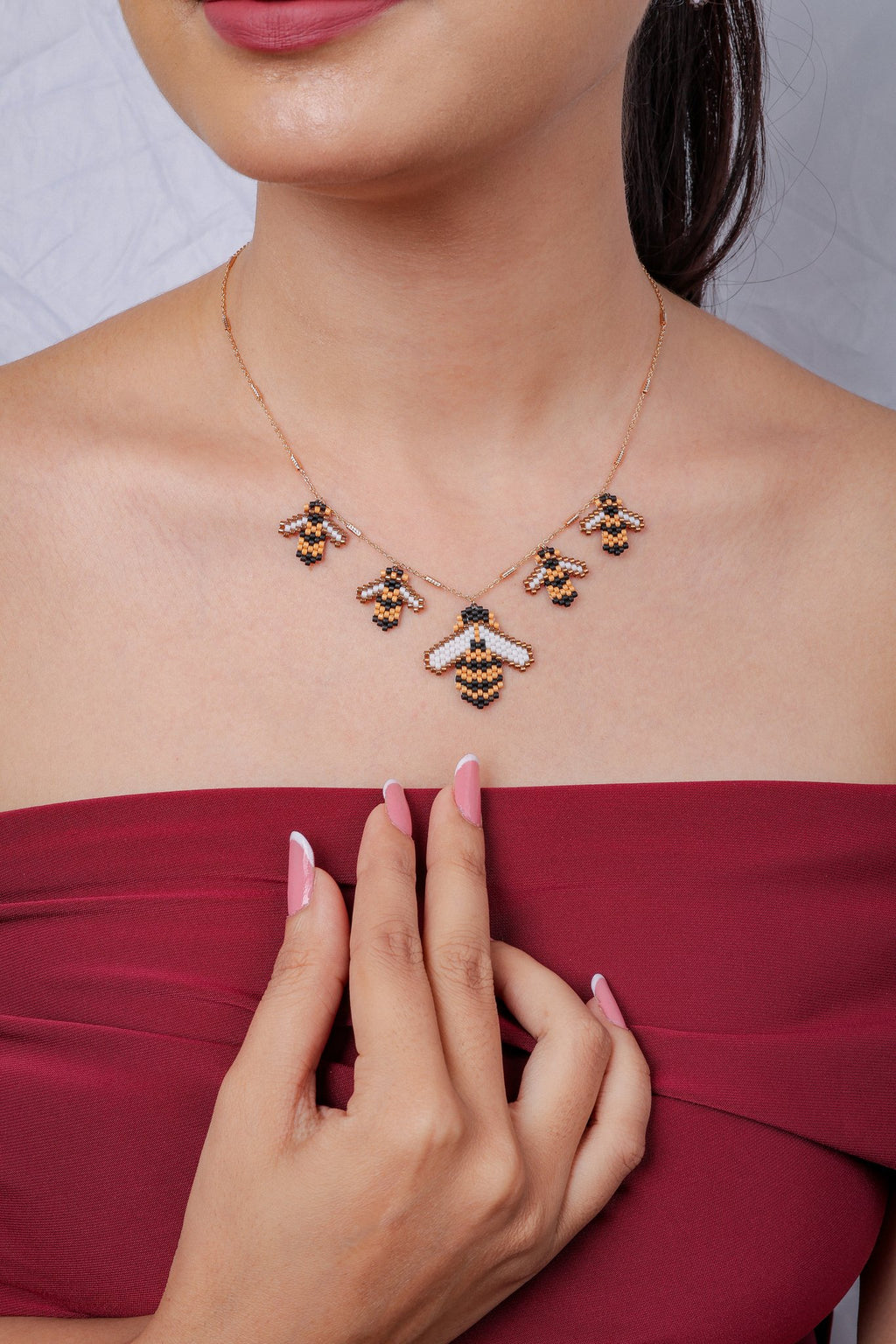Model with hand on chest wearing rose-gold necklace of five striped beaded bees