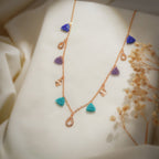 Rose-gold chain necklace with cobalt, purple and turquoise beaded triangle charms on cream fabric