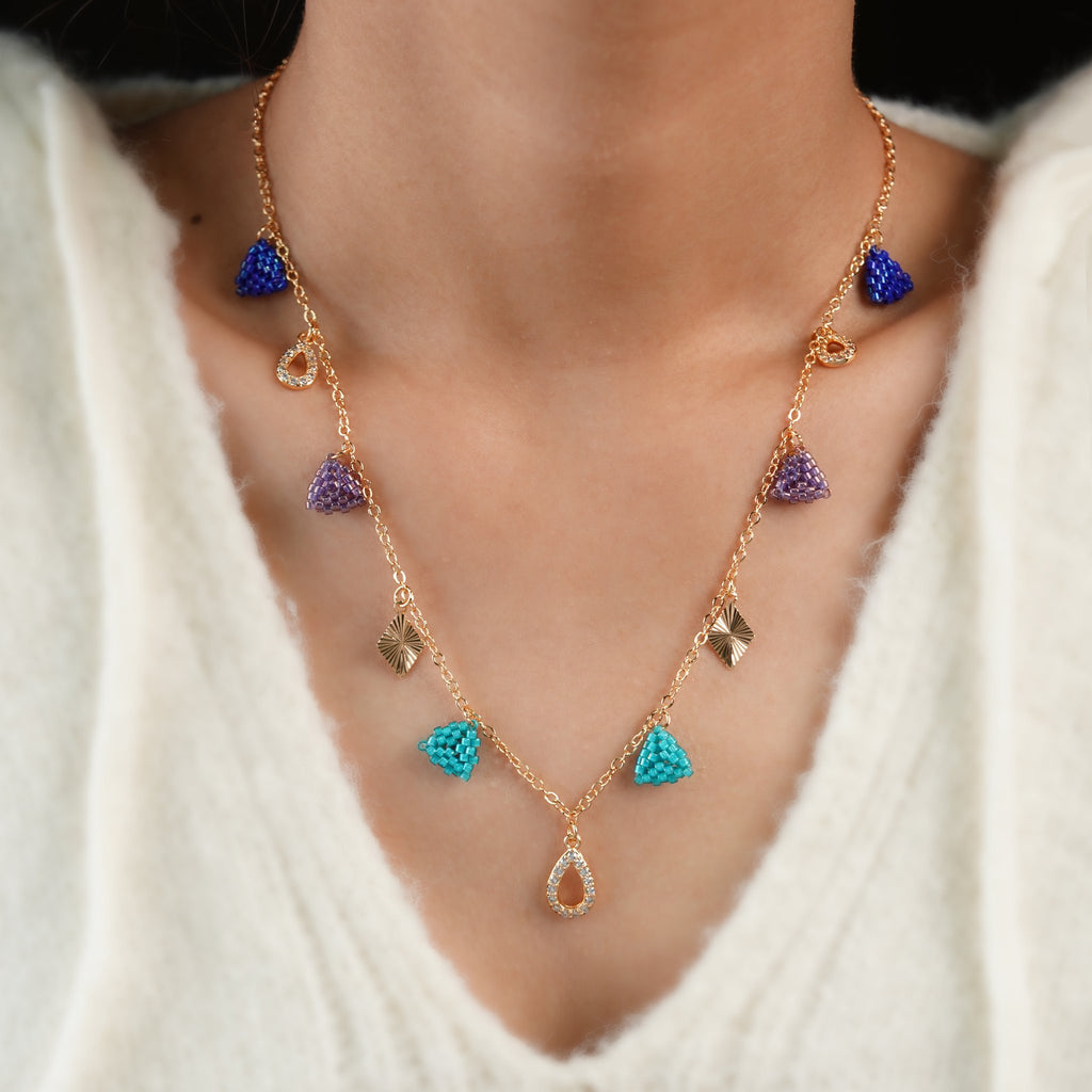 Model wearing rose-gold charm necklace with jewel-tone beaded triangles and a crystal teardrop drop