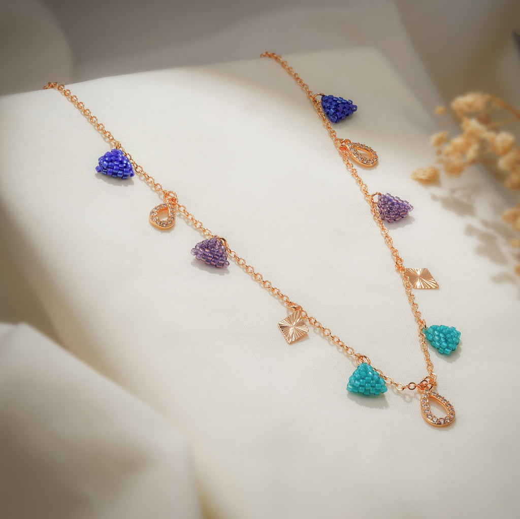 Angled view of beaded triangles, crystal teardrops and sunburst diamond charms on a rose-gold chain