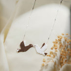 Silver chain necklace with brown and white beaded doves meeting beak to beak on cream silk