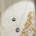 Silver chain necklace with white pixel-beaded cat charm and black and white paw-print charm on cream