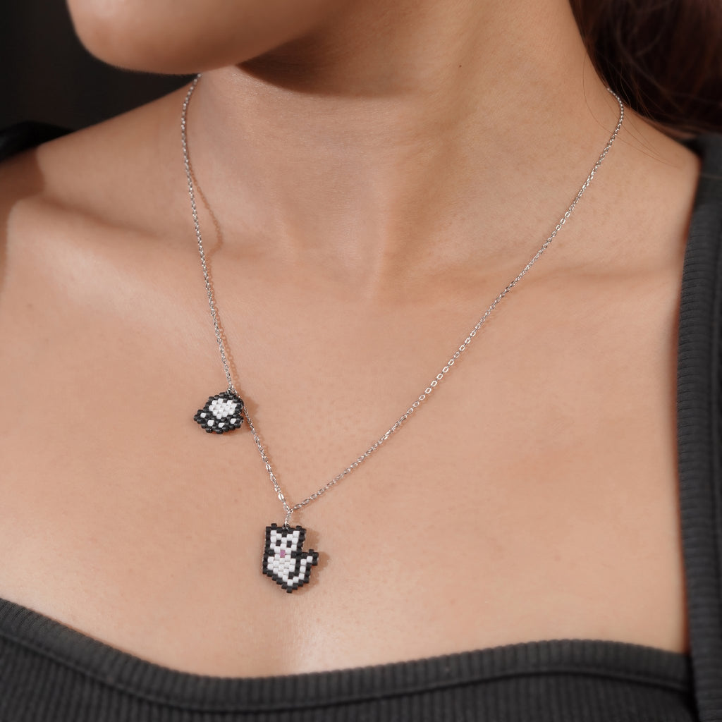 Model wearing silver necklace with black and white beaded kitty charm and paw-print charm