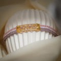Lilac, pink and white woven bead bracelet with gold crystal-set centre plate on a ribbed stand
