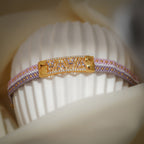 Lilac, pink and white woven bead bracelet with gold crystal-set centre plate on a ribbed stand