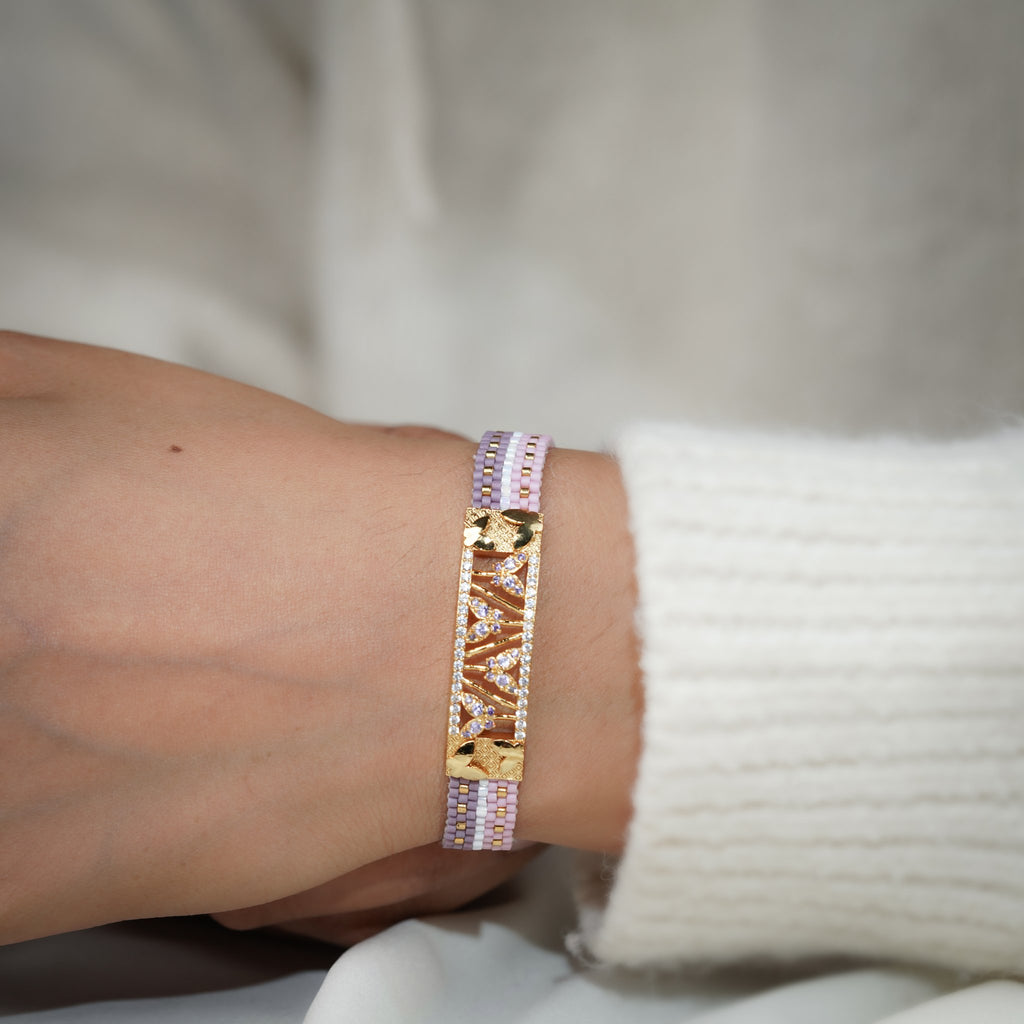Woven lilac bead bracelet worn on the wrist with gold openwork centre plate