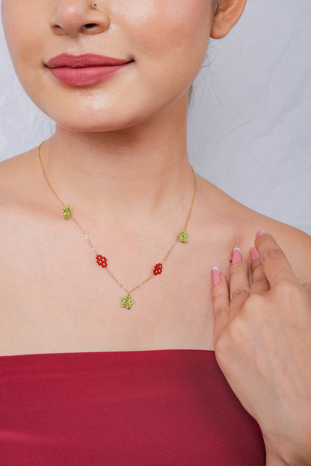 Gold chain necklace with lime-green beaded stars and red beaded diamond stations at the neckline