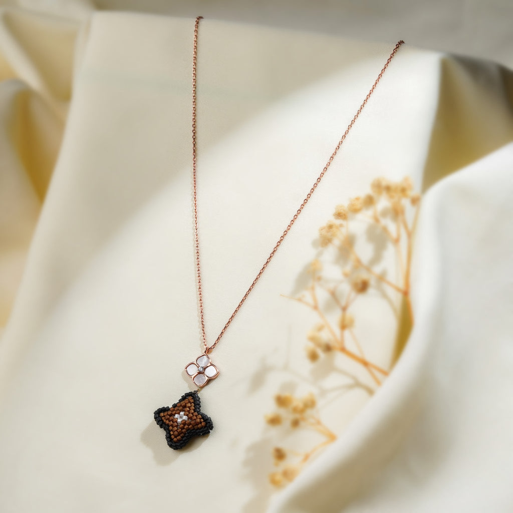 Rose-gold necklace with pearly four-petal flower and black and brown beaded clover pendant on cream fabric