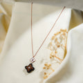 Rose-gold necklace with pearly four-petal flower and black and brown beaded clover pendant on cream fabric