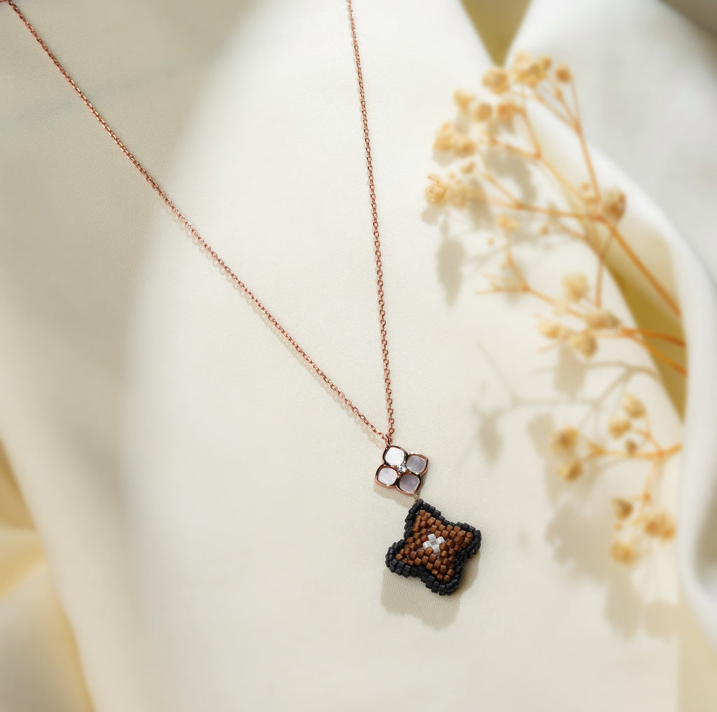 Close view of black-edged brown beaded clover pendant hanging from rose-gold flower connector
