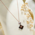 Close view of black-edged brown beaded clover pendant hanging from rose-gold flower connector
