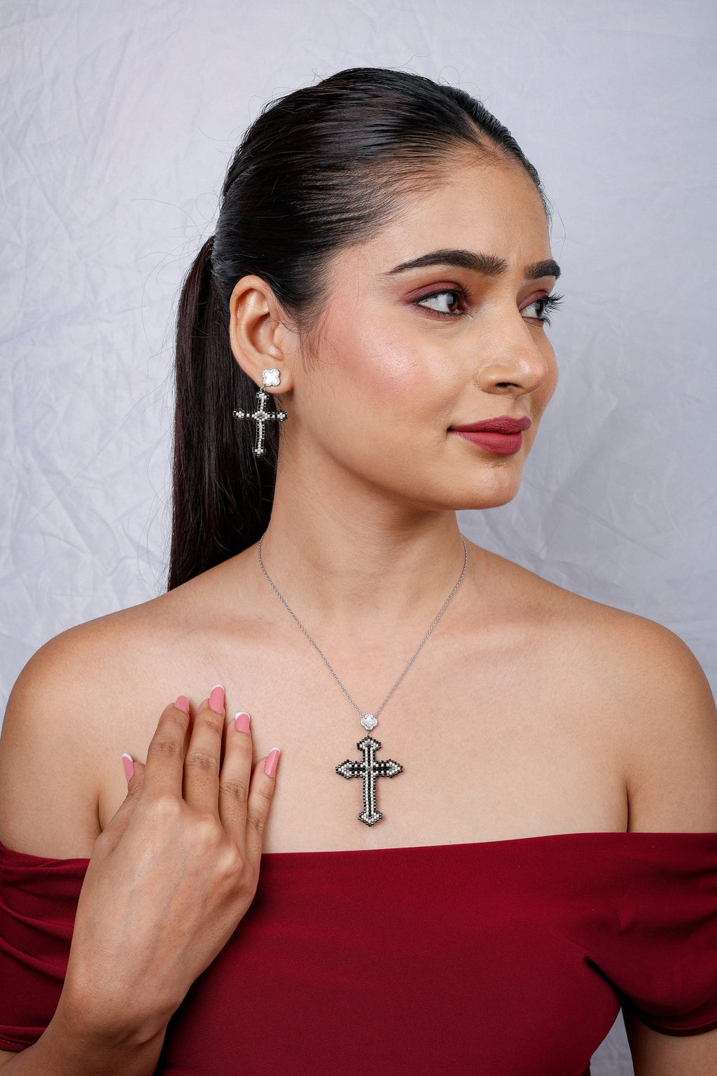Model in red off-shoulder top wearing beaded cross pendant and cross drop earrings