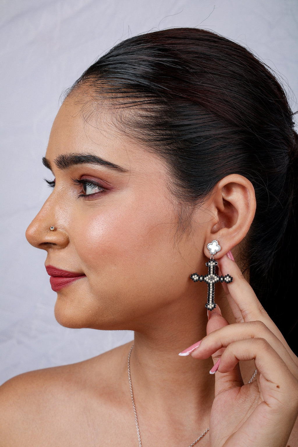 Close profile of beaded cross drop earring on a pearly clover stud with crystal border