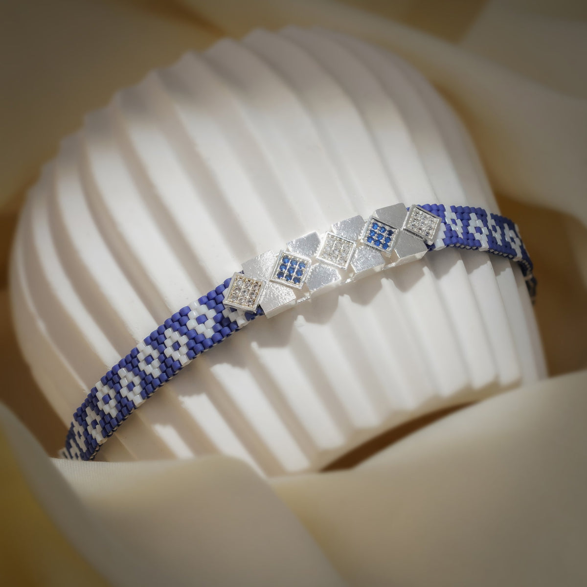 Woven cobalt bracelet with clear and blue crystal squares curved over a ribbed stand