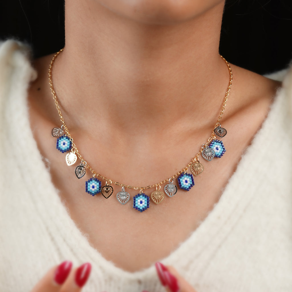 Model wearing an evil-eye and heart charm necklace over a cream knit sweater